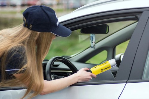 Officer holding a roadside breathalyzer toward a driver through an open car window